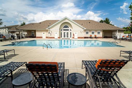 A pool with a building behind it and chairs in front.