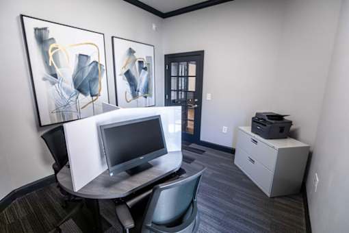 A room with a desk, chair, and two framed artworks on the wall.