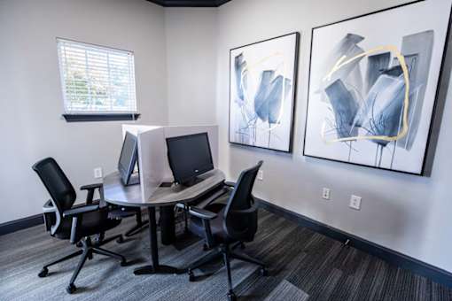 A room with a table, chairs and two computers.