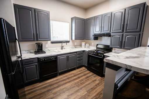 A kitchen with black cabinets and a wooden floor.
