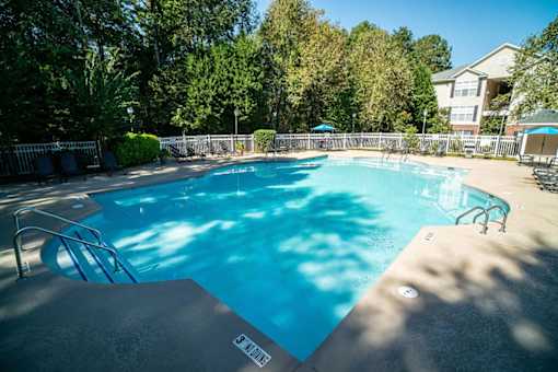A swimming pool surrounded by trees and a building in the background.