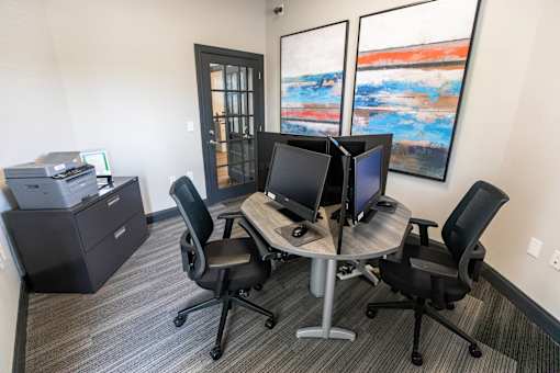 A room with a desk and chairs and a painting on the wall.