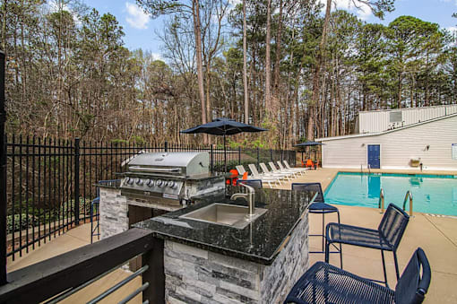 A black grill is on a stone patio next to a pool.