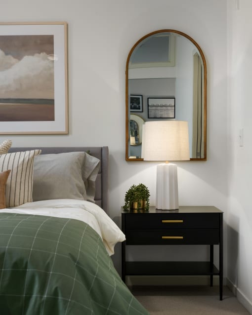 a bedroom with a bed and a nightstand with a lamp and a mirror