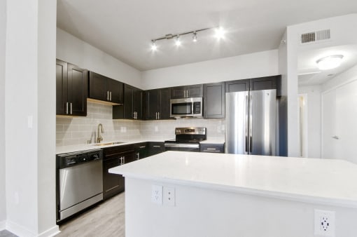 Renovated kitchen with stainless steel appliances, custom espresso cabinetry, designer tile backsplash, kitchen island, and white marble countertops