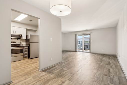 A spacious room with wooden flooring and a kitchen area in the background.