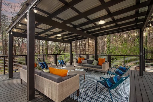 A wooden deck with a sofa and chairs under a roof.