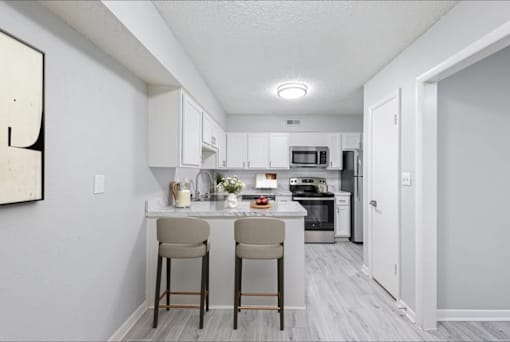 A kitchen with white cabinets and a white countertop with two bar stools.