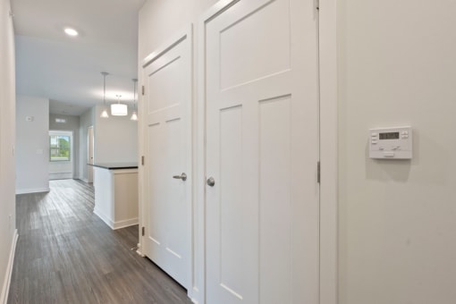 a white hallway with white closets and a kitchen