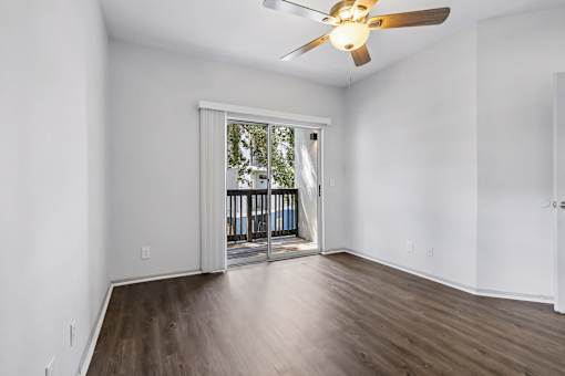 A room with a ceiling fan and sliding glass doors leading to a balcony.
