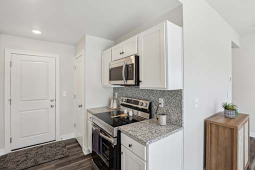 2 Bedroom Townhomes In Blue Springs, MO - Chapman Ridge Townhomes - A Kitchen Features Granite Countertops, White Cabinets, Stainless Steel Oven, Vinyl Plank Flooring, And A Small Potted Plant.