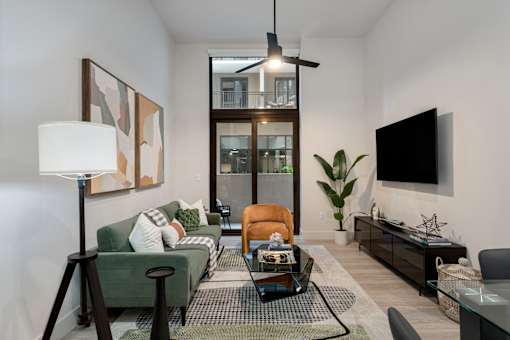 A living room with a green couch, a coffee table, and a flat screen TV mounted on the wall.