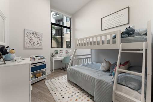 A white bunk bed with a grey bedspread and pillows is in a room with a white dresser and a white rug with black dots.
