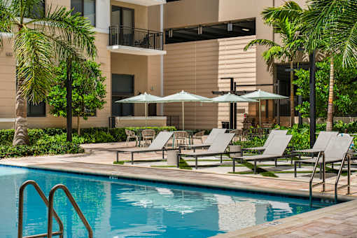 A pool surrounded by lounge chairs and umbrellas in front of a building.