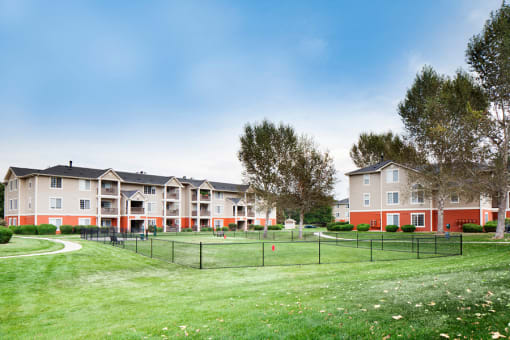 Ardenne Apartments grassy, fenced in dog park with community buildings behind it.