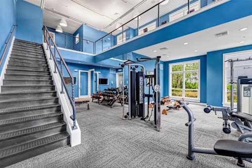 A gym with a staircase, exercise equipment, and windows.