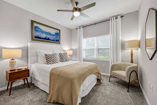 A bedroom with a large bed, a ceiling fan, and a painting on the wall.
