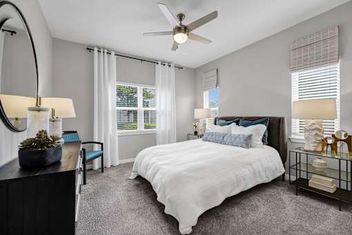 A bedroom with a large bed, a ceiling fan, and a window with blinds.