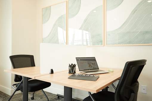 A laptop is open on a table with a black chair on either side.