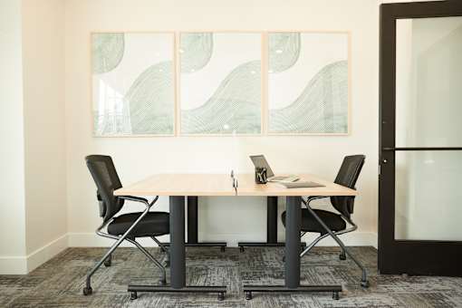 A conference room with a table, chairs, and a painting on the wall.