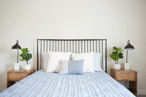 A bed with a blue comforter and pillows is flanked by two small tables with plants on them.
