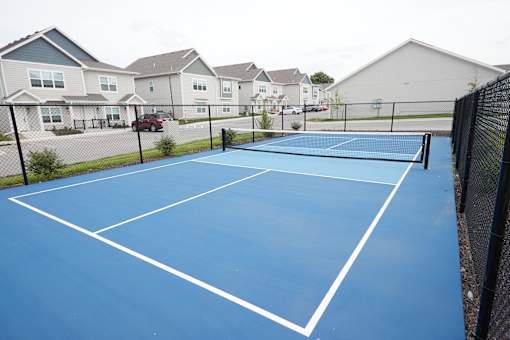 A blue tennis court with white lines and a black fence.