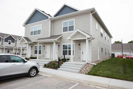 A white car is parked in front of a two-story house.