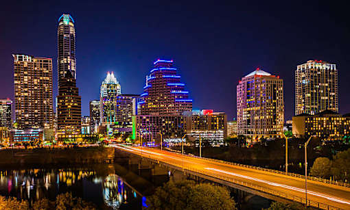 A city skyline at night with a bridge and lights reflecting in the water.