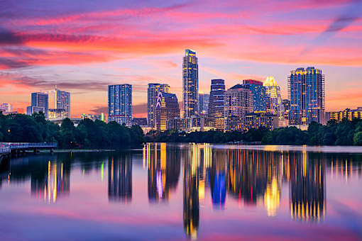A city skyline is reflected in a body of water at sunset.