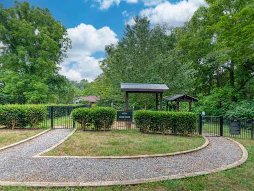A small pavilion is surrounded by a hedge and a gravel path.