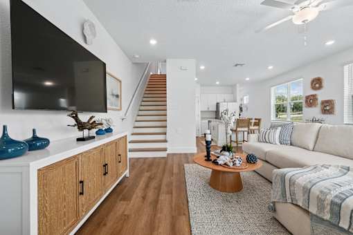 A living room with a white couch, wooden floors, and a staircase in the background.
