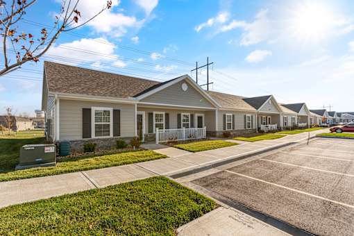  Dog-Friendly Senior Townhomes in Belton, MO - Traditions Villas 55+ - An Off-Street Parking Area Fronting a Row of Houses with Fences and Yards.