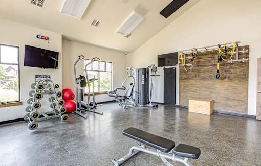 A gym with a variety of equipment including a bench, weights, and a television.