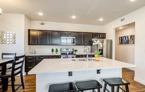 A modern kitchen with a white island and black chairs.
