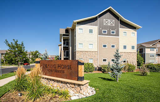 A sign in front of a building that says "Bucking Horse Apartments".