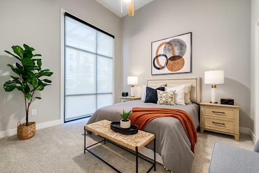 A bedroom with a bed, nightstand, and a plant.