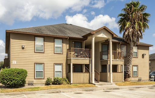 A two-story apartment building with a balcony and a palm tree in front.