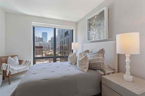 A bedroom with a large bed, a chair, and a view of the city.