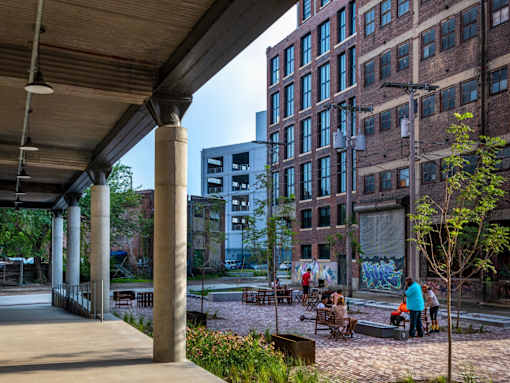 A group of people are sitting and standing on a patio under a covered walkway.