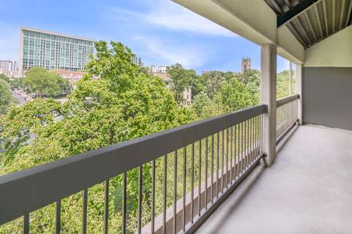 A balcony with a metal railing overlooks a cityscape with buildings and trees.