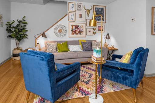A living room with a grey couch, two blue velvet chairs, and a patterned rug.