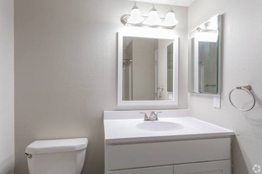 A white bathroom with a sink, toilet, and mirror.