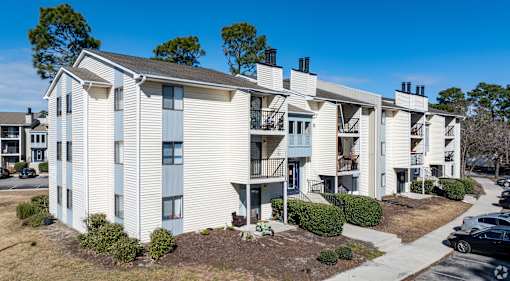 A row of white apartment buildings with balconies and a clear blue sky above.