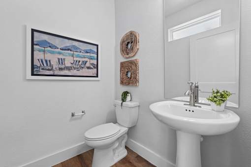 A bathroom with a toilet, sink, and a painting of a beach scene on the wall.