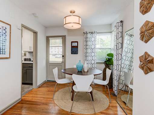A dining room with a table surrounded by chairs and a rug on the floor.