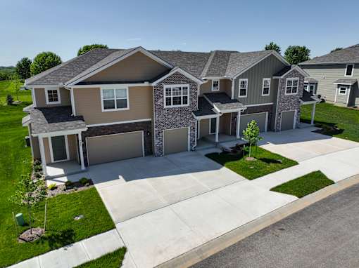 A large, modern house with a grey roof and a stone pillar in the front yard.