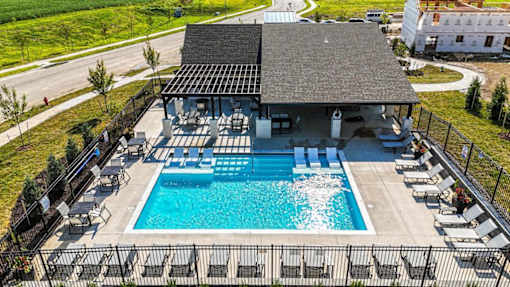 A large outdoor swimming pool with lounge chairs and a building with a black roof.