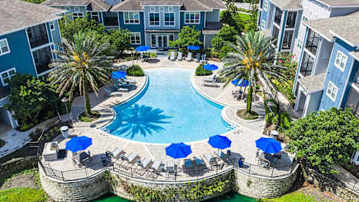 A swimming pool surrounded by a stone wall and blue umbrellas.