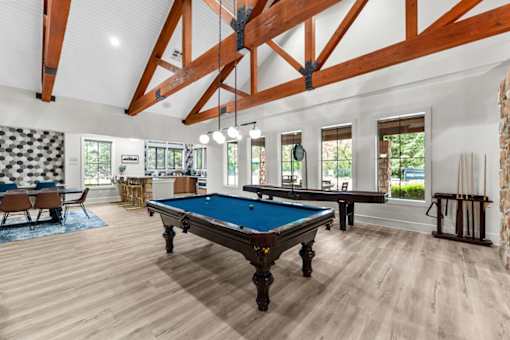 A pool table is in the middle of the clubhouse with wooden floors and a high ceiling.