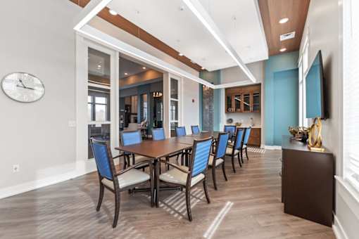 Shawnee, KS Apartments Near Kansas Speedway - Bonavia Luxury Apartments - Clubhouse Dining Room with Long Table, Chairs, Storage Cabinets, and Wall-Mounted TV.